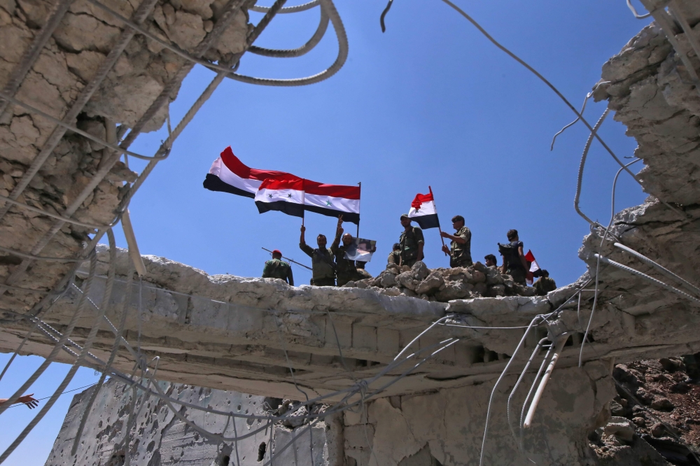 Syrian government forces' soldiers wave their national flags after taking back the city of Quneitra to the rebels, on July 19, 2018. Under pressure, rebels have agreed to hand over Quneitra and the buffer to government forces, an opposition negotiator and