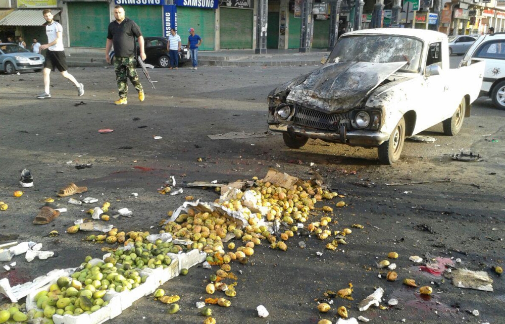 A handout picture released by the official Syrian Arab News Agency (SANA) on July 25, 2018 shows a member of the Syrian security forces walking past a truck damaged in a suicide attack in the southern city of Sweida. (AFP PHOTO / HO / SANA)