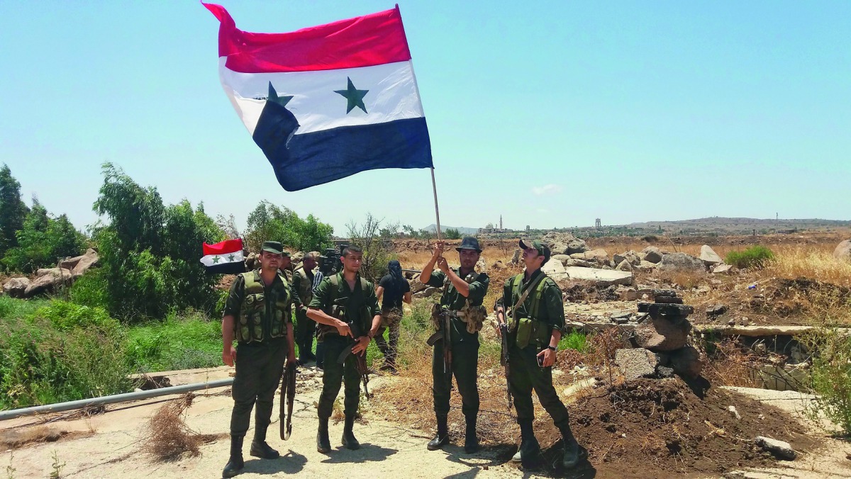 A handout picture released by the official Syrian Arab News Agency (SANA) on July 26, 2018 shows Syrian army soldiers carrying the national flag in the village of Hamidiya in the southern province of Quneitra.  AFP /SANA