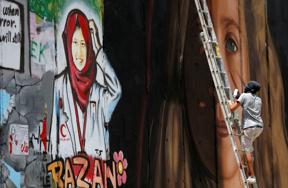 A foreign artist paints on the Israeli wall a mural depicting Palestinian teen Ahed Tamimi who is detained by Israel, next to a mural of dead Palestinian nurse Razan Al-Najar, in Bethlehem, in the occupied West Bank, July 25, 2018. Reuters/Mussa Qawasma
