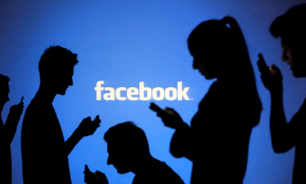 People are silhouetted as they pose with mobile devices in front of a screen projected with a Facebook logo, in this file picture. (REUTERS/Dado Ruvic/File Photo)