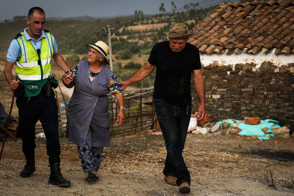 A Police officer evacuates locals due to a wildfire close to Monchique in the Portuguese Algarve, on August 4, 2018.  AFP / Carlos Costa
 