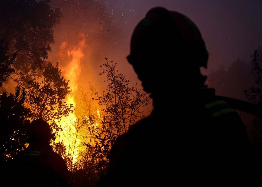Firefighters watch trees burning in flames as they combat a wildfire close to Monchique in the Portuguese Algarve, on August 8, 2018.  / AFP / CARLOS COSTA 