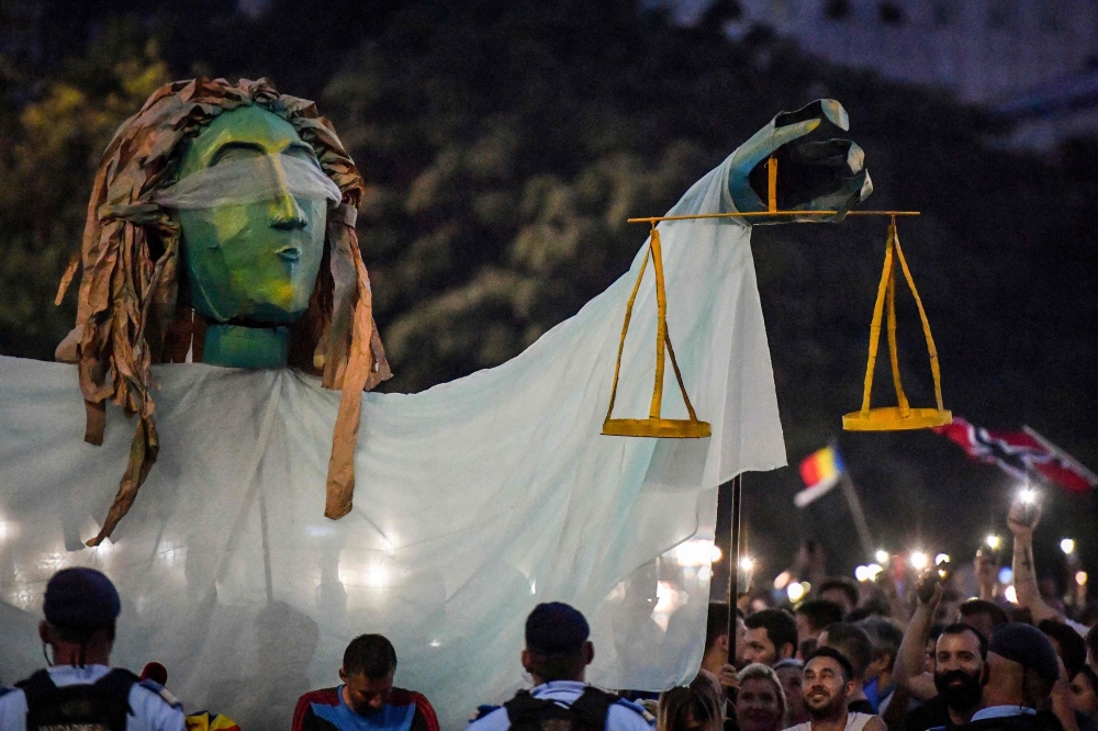 Romanians chant slogans as they stand next to a giant statue picturing the symbol of justice during a demonstration to protest against the government on August 11, 2018, in Bucharest. AFP / Daniel Mihailescu
 