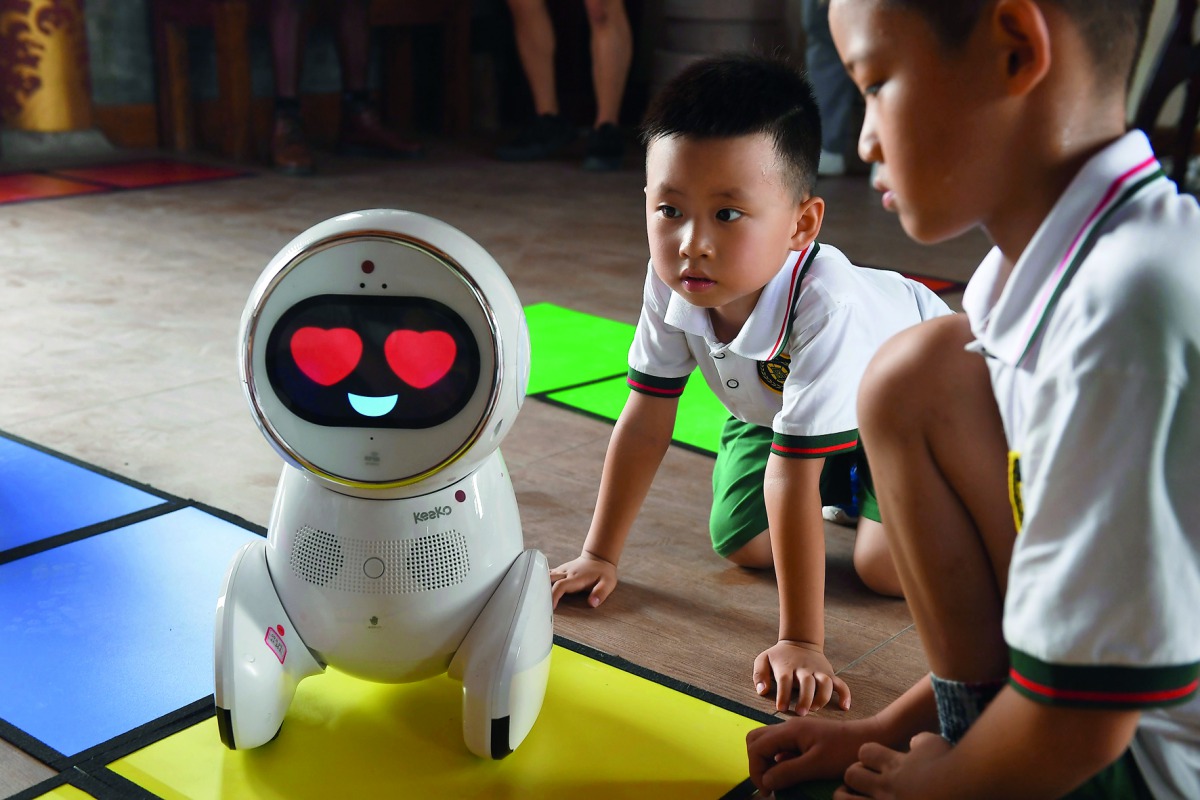 This photo taken on July 30, 2018 shows children watching a Keeko robot make its way on a path they made from square mats at the Yiswind Institute of Multicultural Education in Beijing. AFP / Greg Baker 