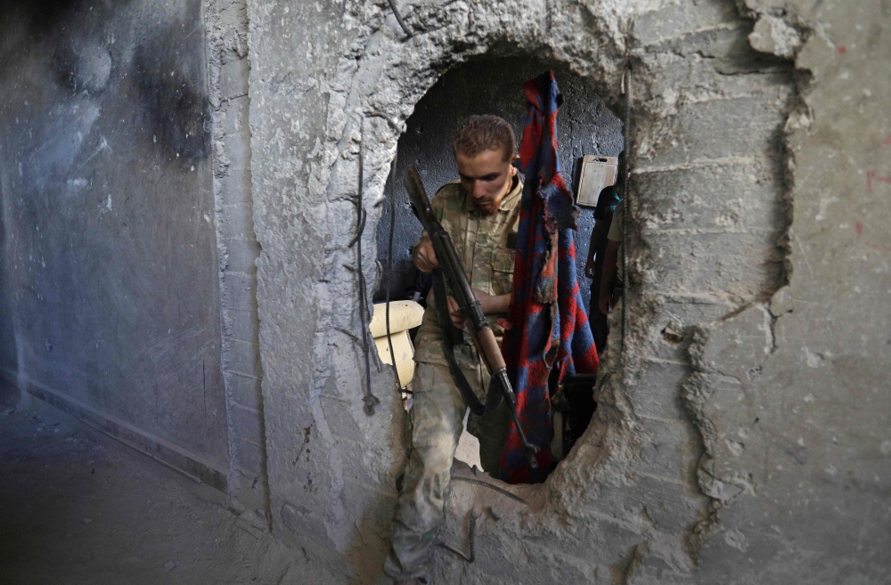 A Syrian rebel fighter who was displaced from Ghouta in the Damascus province earlier this year steps out through a hole in a damaged building in a rebel-held neighbourhood on the western outskirts of Aleppo in northern Syria on September 10, 2018.   AFP 
