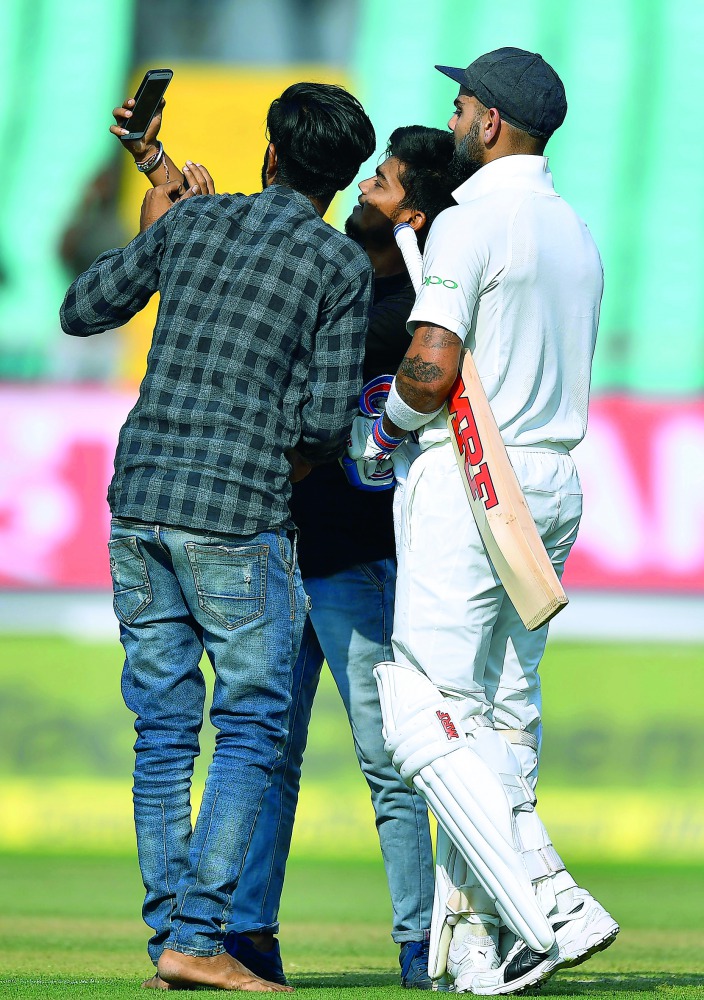 Indian cricket captain Virat Kohli (R) poses for a selfie with fans, as they invaded the field, during the first day's play of the first Test cricket match between India and West Indies at the Saurashtra Cricket Association stadium in Rajkot on October 4,