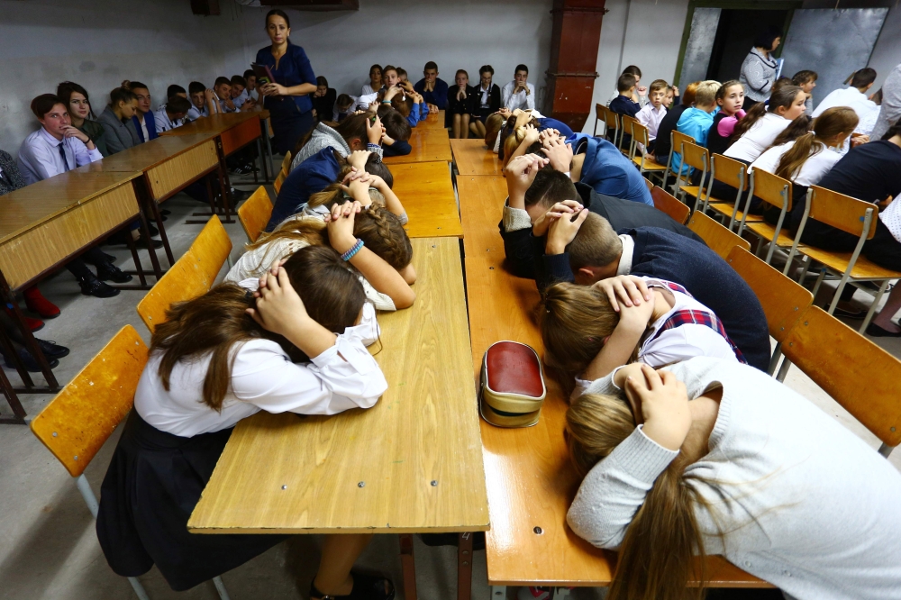 Schoolchildren cover their heads with their hands as they take part in security exercises in the school in the Kiev-controlled village of Sartana, Donetsk region on October 2, 2018. AFP / Aleksey FILIPPOV