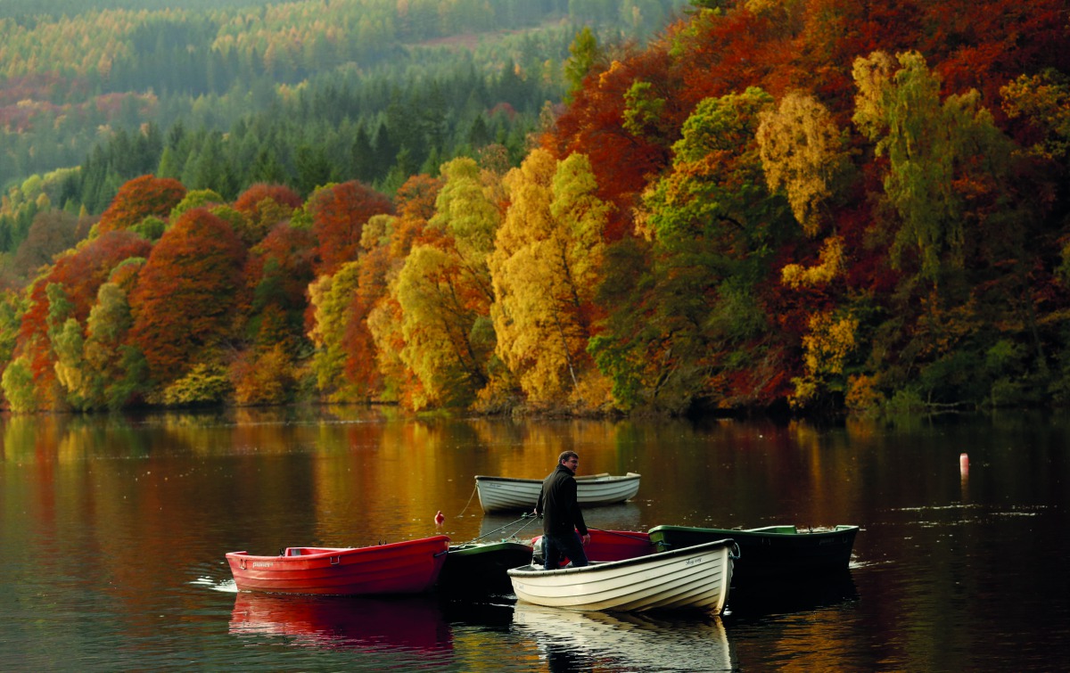 A man stands on a boat as autumn foliage is reflected off Loch Faskally, in Perthshire, Scotland, Britain, October 19, 2018. Reuters/Russell Cheyne