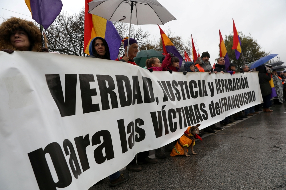 A dog wearing a Spanish Republican flag around its neck stands by a banner that reads 