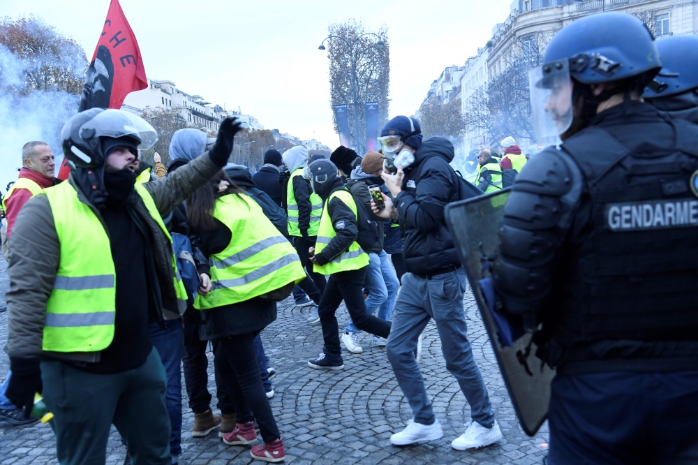 A Yellow vest (Gilet jaune) demonstrator gestures next to a gendarme on the Champs Elysees in Paris, on November 24, 2018, during a protest against rising oil prices and living costs. AFP / Bertrand Guay