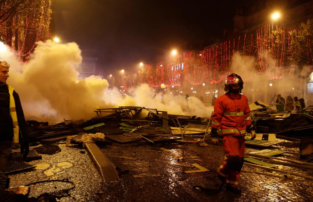 A yellow vest (Gilets Jaune) protestor looks on as a firefighter walks amongst extinguished burning material near The Arc de Triomphe on the Champs Elysees in Paris, on November 24, 2018, during a rally by yellow vest protestors against rising oil prices 