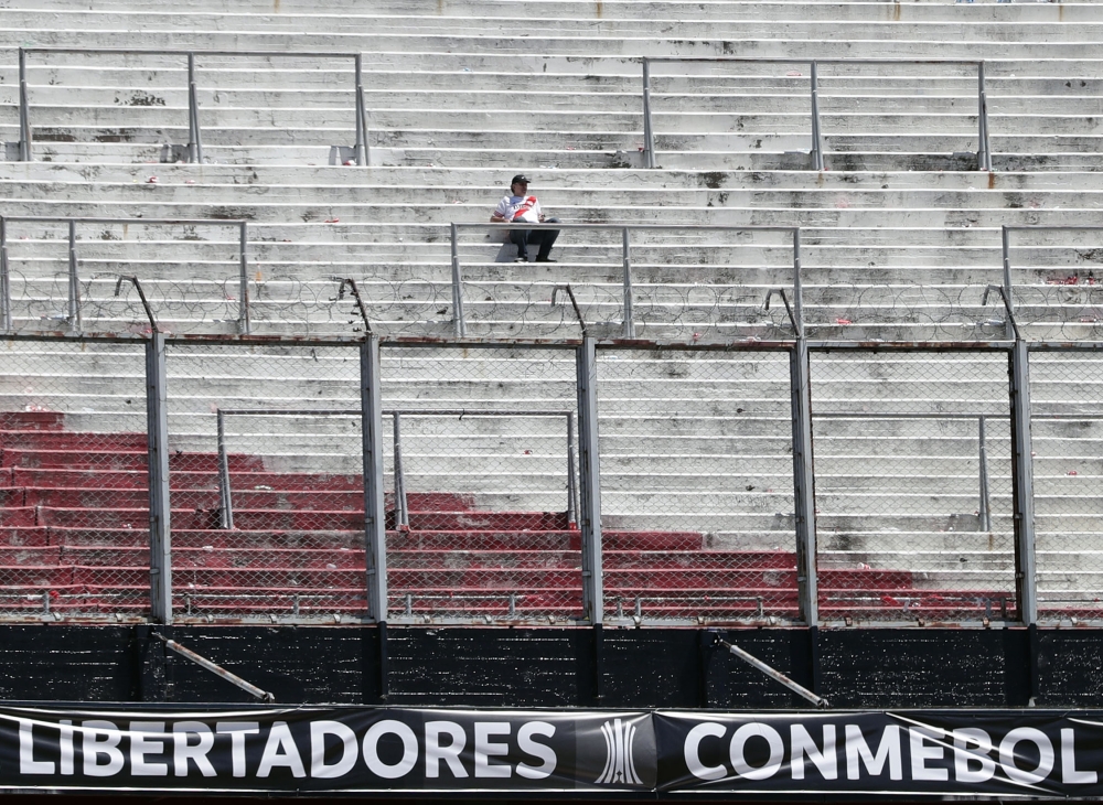 A supporter of River Plate sits on an empty stand at the Monumental stadium in Buenos Aires, after the all-Argentine Copa Libertadores second leg final match against Boca Juniors was postponed on November 25, 2018.   AFP / ALEJANDRO PAGNI