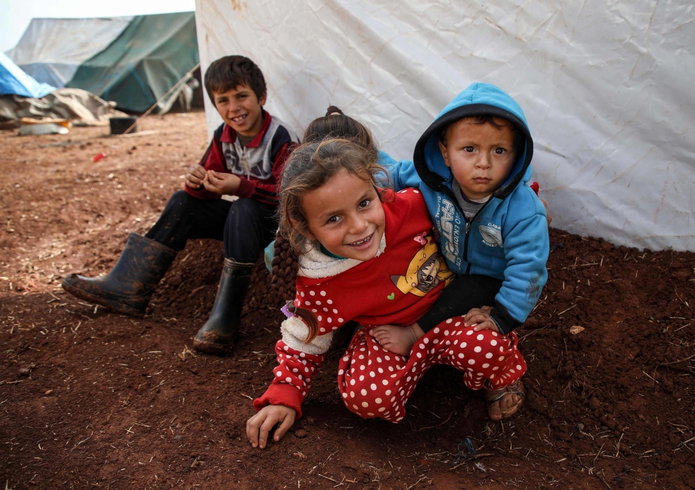 A Syrian girl holds another child as they sit with two others outsid ea tent at a camp for the displaced near the town of Sarmada in the northern countryside of the rebel-held Idlib province on December 1, 2018. AFP / Aaref Watad
 