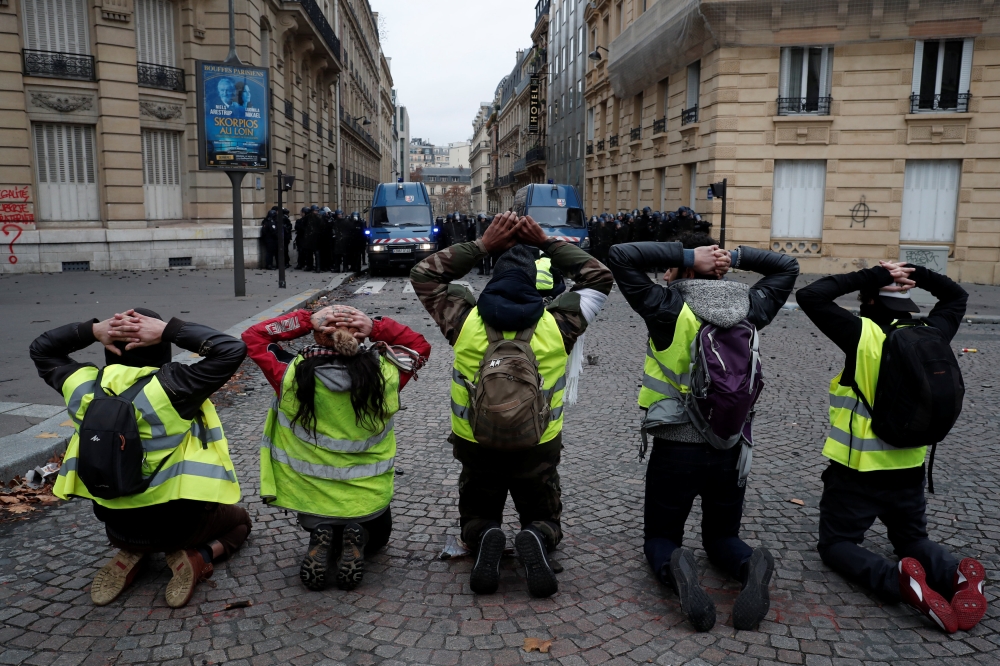 Protesters wearing yellow vests kneel in front French riot police near the Champs-Elysees Avenue at a demonstration by the 