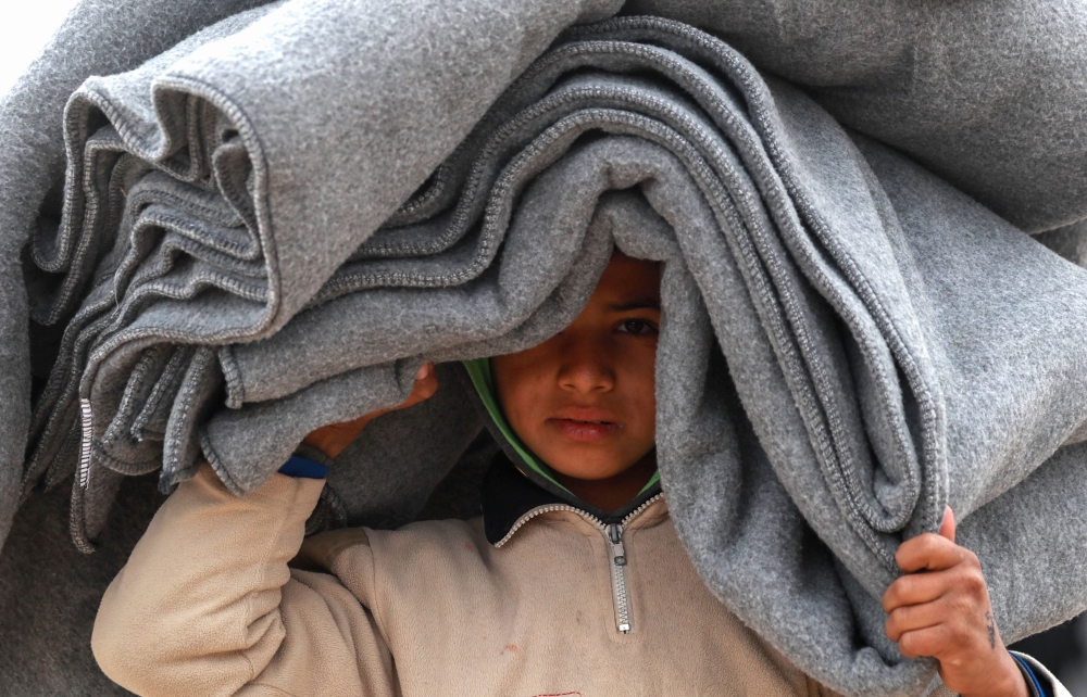 A Syrian displaced boy carries blankets over his head inside the Internallly Displaced Persons (IDP) camp of al-Hol in al-Hasakeh governorate in northeastern Syria on December 8, 2018.   AFP / Delil SOULEIMAN
