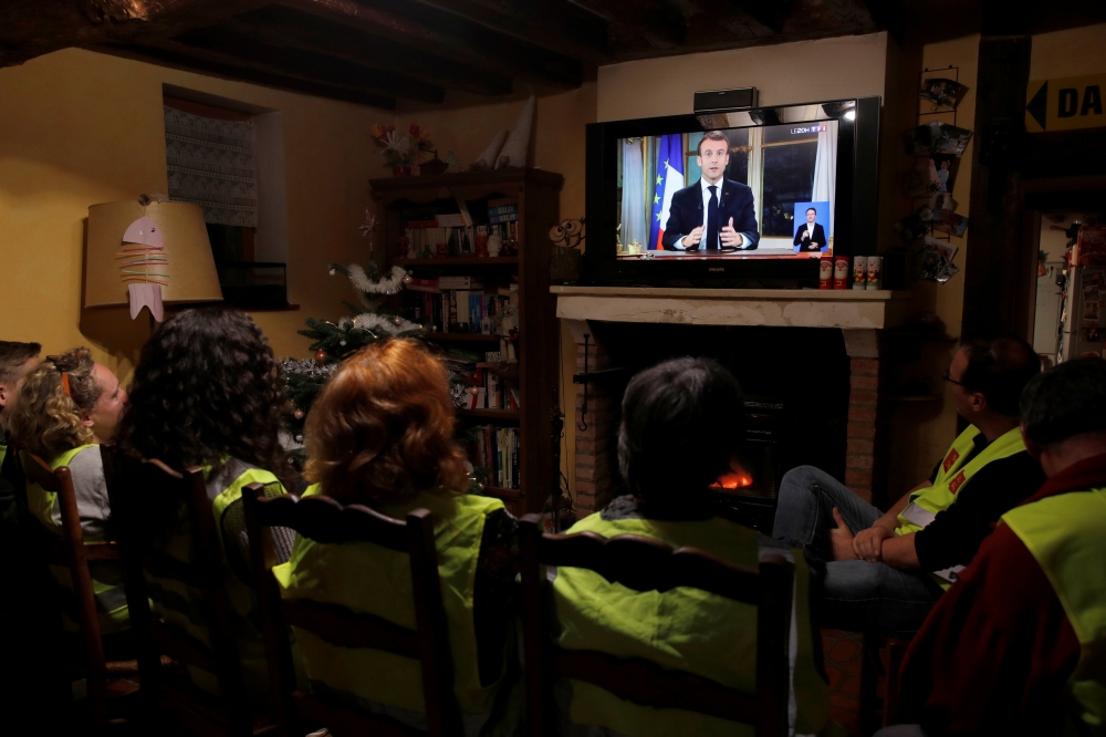 Protesters wearing yellow vests watch French President Emmanuel Macron who addresses the nation about the 