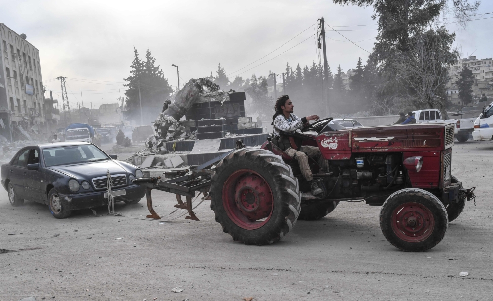 A Turkish-backed Syrian Arab fighter tows a looted vehicle with a tractor after seizing control of the northwestern Syrian city of Afrin from the Kurdish People's Protection Units (YPG) on March 18, 2018. AFP / BULENT KILIC