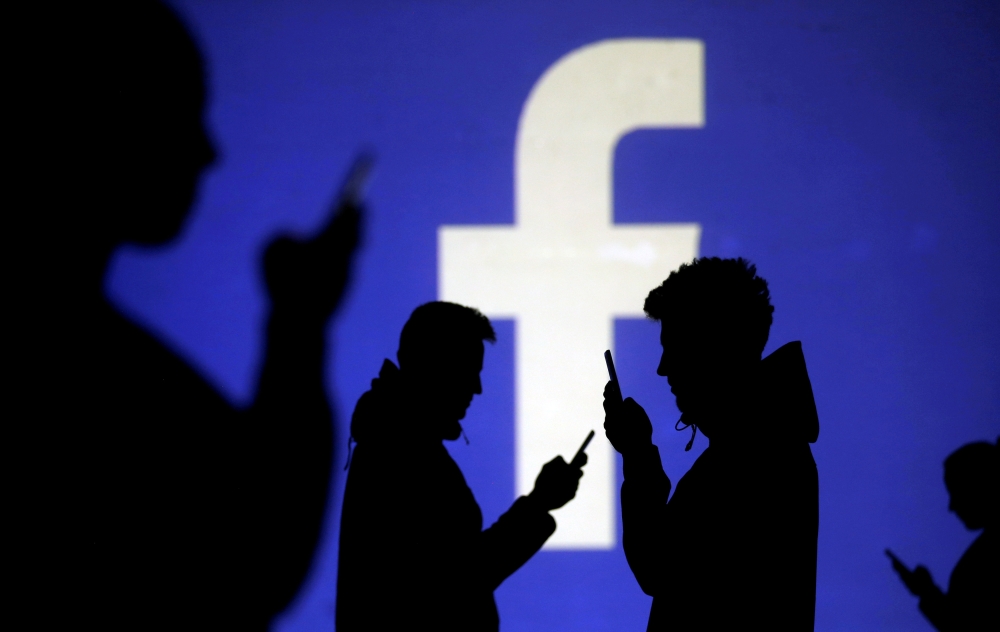FILE PHOTO: Silhouettes of mobile users are seen next to a screen projection of Facebook logo in this picture illustration taken March 28, 2018. REUTERS/Dado Ruvic/Illustration