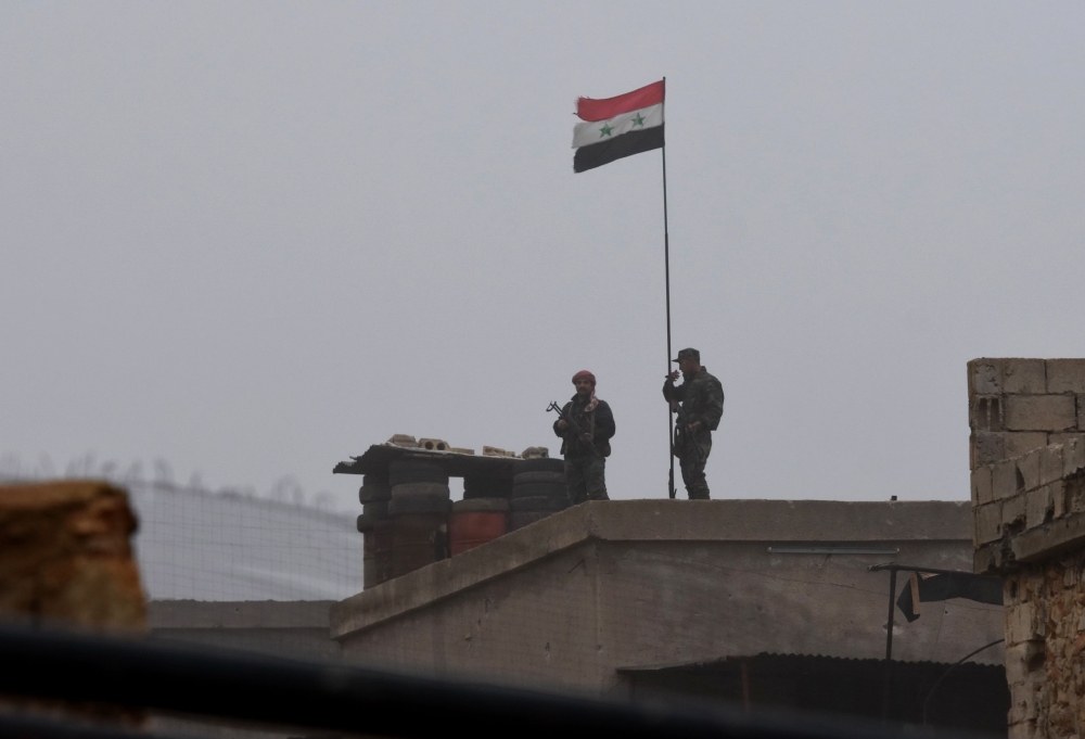 A picture taken on December 30, 2018, shows a Syrian national flag flying over a building as regime forces gather in the southern countryside of the northern Kurdish-controlled city of Manbij. AFP 