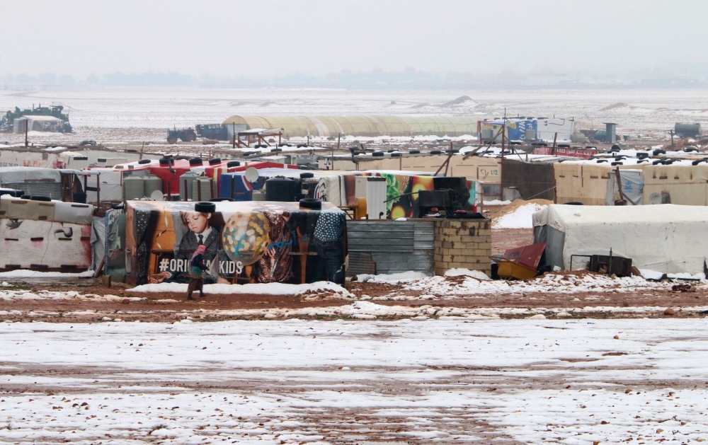 A Syrian refugee walks past makeshift shelters in an unofficial camp for refugees in Iaat in Lebanon's Bekaa valley, a snow storm on January 8, 2019.  / AFP