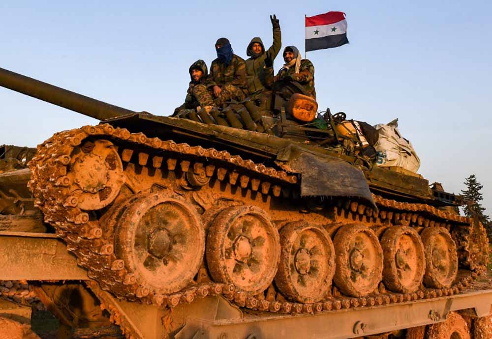 A Syrian soldier flashes the victory gestures as he sits with comrades atop a tank being transported near the northern town of Manbij, on January 12, 2019.  AFP / George OURFALIAN