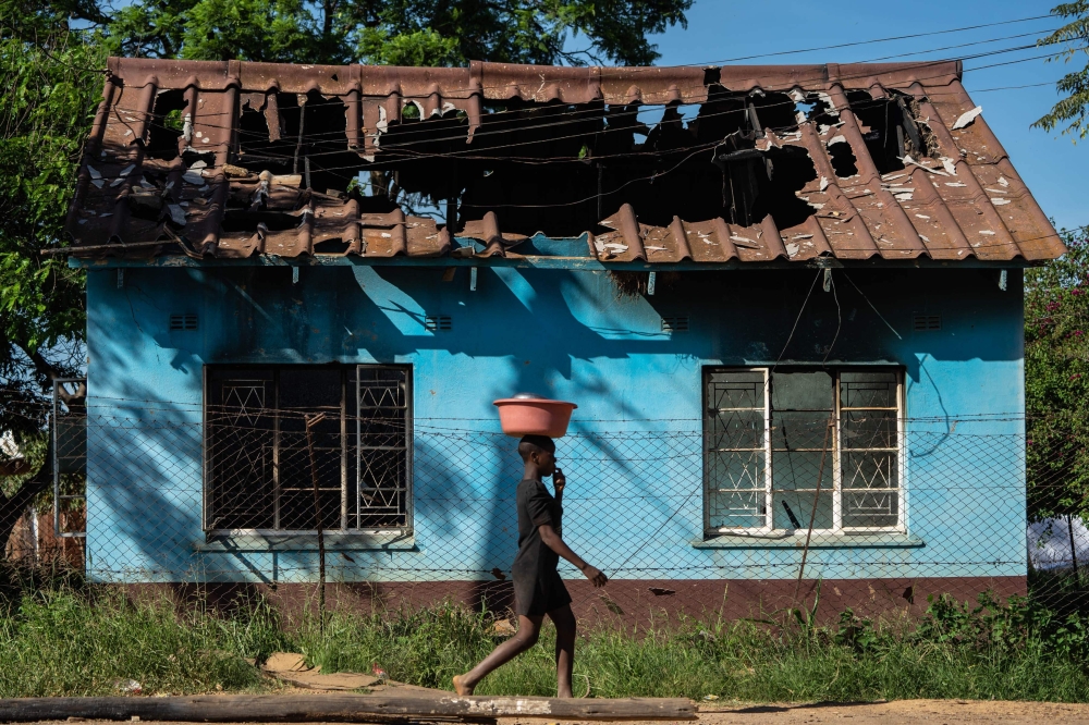 A young woman carries a bowl on her head as she walks past the shell of the burnt-out offices belonging to the ruling ZANU PF party's Kadoma district in Rimuka township, Kadoma on January 24, 2019. / AFP / ZINYANGE AUNTONY 