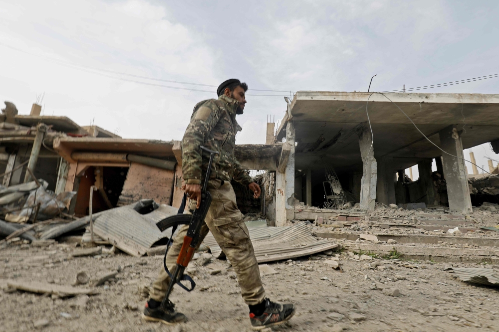 A fighter from the Syrian Democratic Forces (SDF) walks past a former Islamic State (IS) group jihadist alms tax centre in the city of Hajin in Syria's eastern Deir Ezzor province on January 27, 2019 after the Kurdish-led and US-backed SDF retook the city