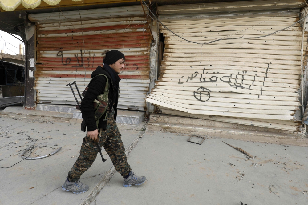 A fighter from the Syrian Democratic Forces (SDF) walks past shops with their fronts painted with the Arabic phrases 