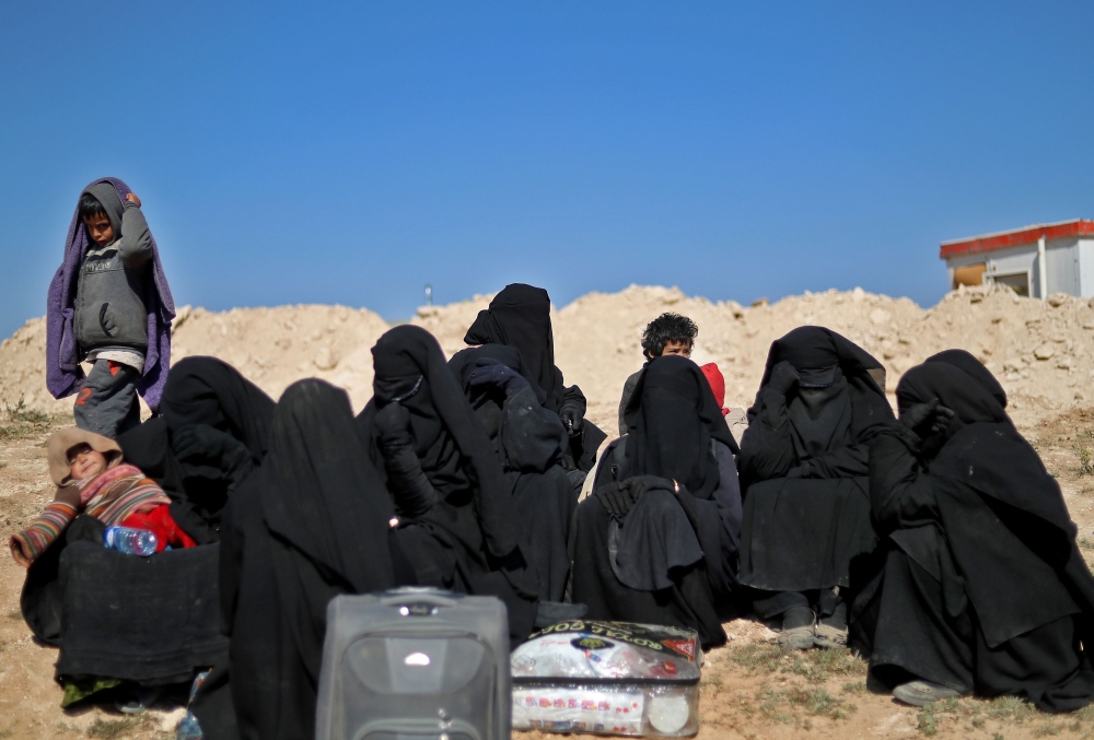 Women wearing niqabs (full face veils) wait as men are being screened by members of the Syrian Democratic Forces, while civilians flee from the battered Islamic State-held holdout of Baghouz in the eastern Syrian province of Deir Ezzor into a nearby area 