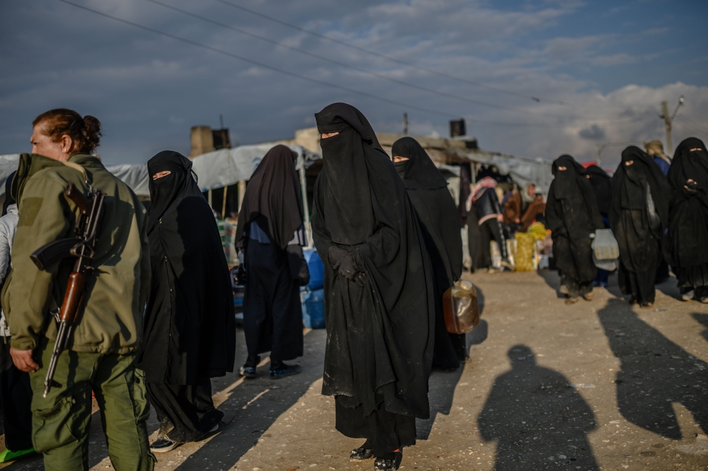 Veiled women, reportedly wives and members of the Islamic State, walk under the supervision of a female fighter from the Syrian Democratic Forces (SDF) at al-Hol camp at al-Hasakeh governorate at northeastern Syria on February 17, 2019. / AFP / BULENT KIL