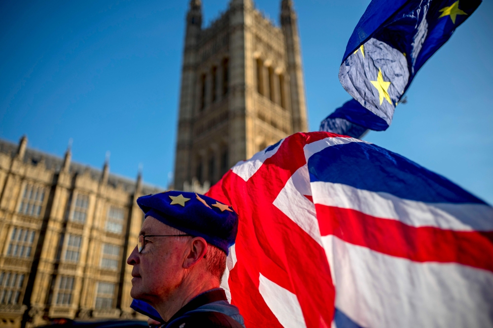 An anti-Brexit protester wearing a European Union flag cap, flies European and Union flags outside the Houses of Parliament in London on February 21, 2019. AFP / Tolga Akmen 