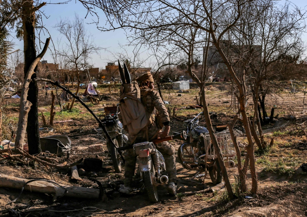 Fighters with the Syrian Democratic Forces (SDF) sits on a motorcycle at a makeshift camp for Islamic State (IS) group members and their families in the town of Baghouz, in the eastern Syrian province of Deir Ezzor, on March 9, 2019. / AFP / Dylan COLLINS