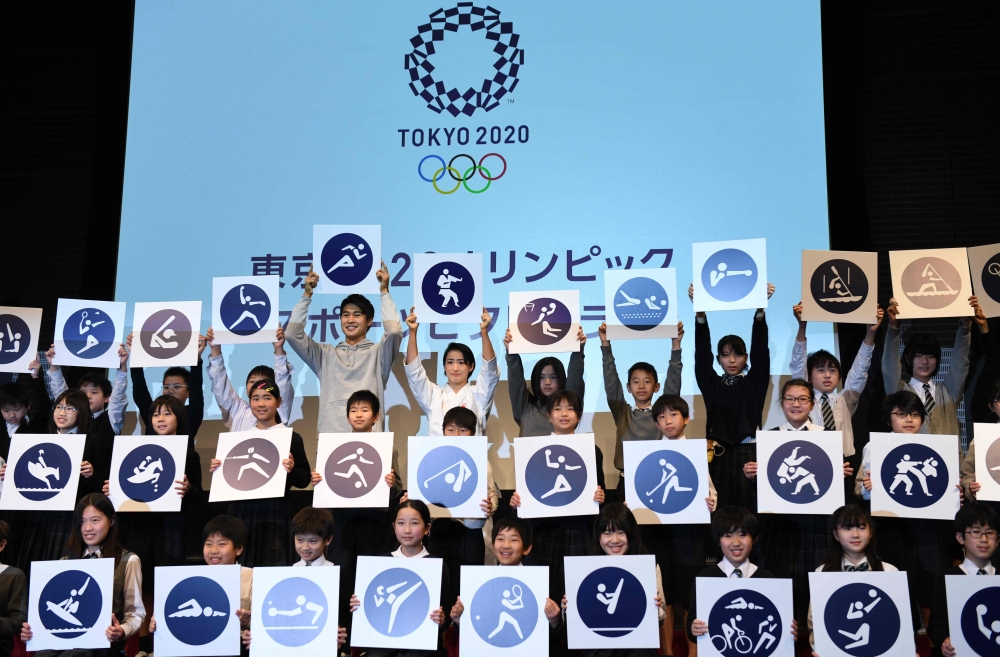 Japan's 4x100 metre relay Rio 2016 silver medallist Shota Iizuka (top row 6th L), national karate team member Kiyo Shimizu (top row 6th L) and elementary school students display sports pictograms for the Tokyo 2020 Olympic Games during an unveiling ceremo