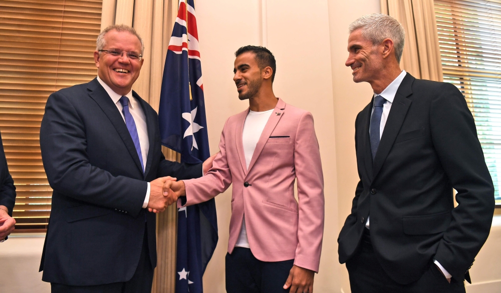 Australia's Prime Minister Scott Morrison (L) shakes hands with Hakeem al-Araibi (C), who was granted refugee status and residency in Australia in 2017 after fleeing Bahrain, next to former Australian football player Craig Foster (R) after al-Araibi becam