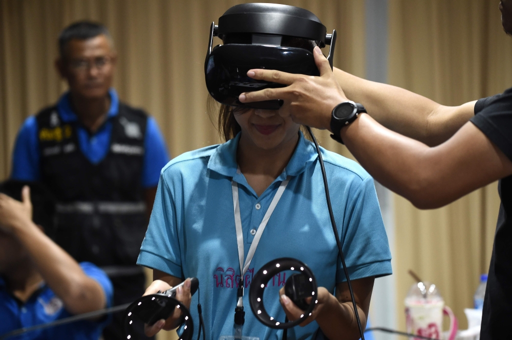 A Thai forensic police officer wearing a virtual reality headset before searching for victims in a simulated city in ruins at the police headquarters in Chon Buri province on February 26, 2019. AFP / Lillian Suwanrumpha 