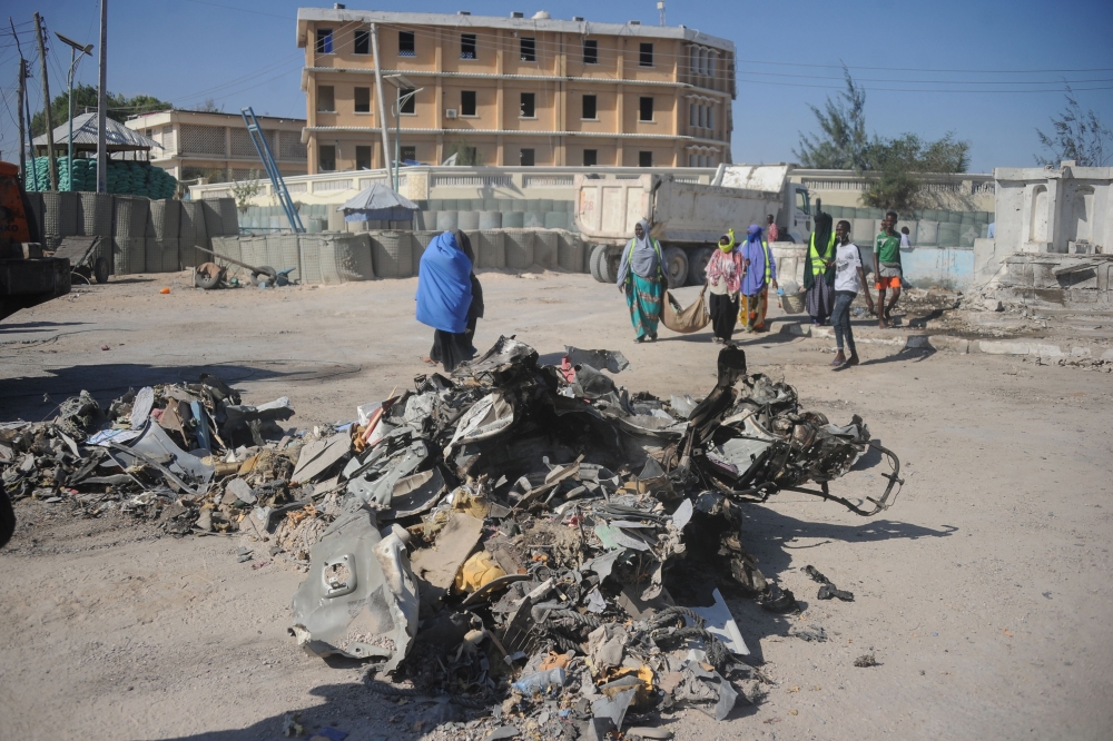 People walk near the wreckage of a car near the complex housing Somalia's ministries of works and labour stormed by Al-Shabaab militants in Somalia's capital Mogadishu on March 23, 2019.  AFP / Mohamed ABDIWAHAB
