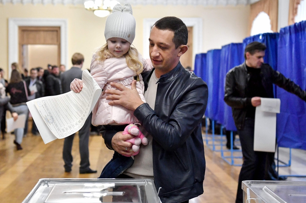 A young girl casts the ballot of a man at a polling station in Kiev on the first round of Ukraine's presidential election, on March 31, 2019.   / AFP / Sergei SUPINSKY