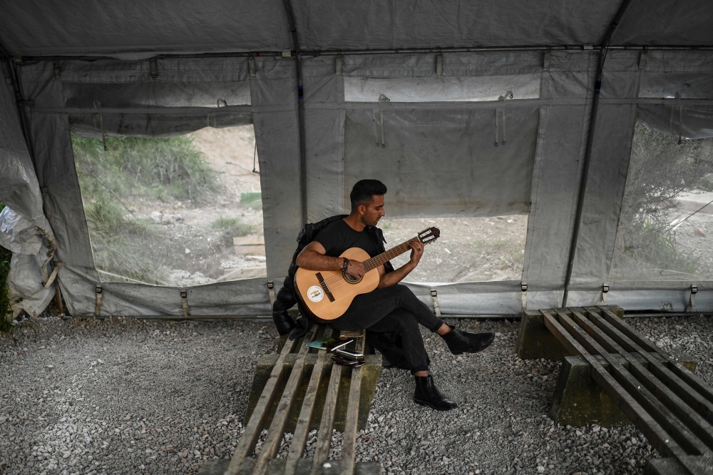  A man plays the guitar at an unofficial camp outside the refugee camp of Moria on the Greek island of Lesbos, on March 19, 2019. AFP / Aris Messinis 