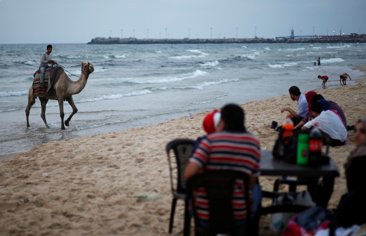 A Palestinian man rides a camel as people sit on a beach on a hot day in Gaza City, July 12, 2017. Reuters/Mohammed Salem