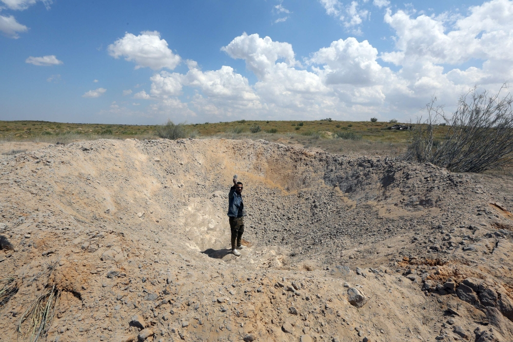 A fighter loyal to Libya's Government of National Accord (GNA) waves from a crater reportedly caused by an air strike west of the city of Aziziah, some 60 kilometres southwest of the capital Tripoli, on April 14, 2019. AFP / Mahmud Turkia
 