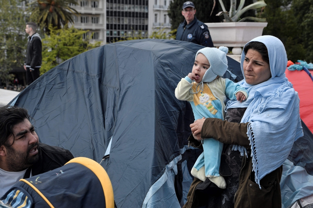 A migrant mother stands by a tent as a group of migrants and refugees camped out at the central Athens Syntagma square, on April 19, 2019, following their eviction from squatted building in Exarchia neibourhood. AFP / Louisa Gouliamaki 