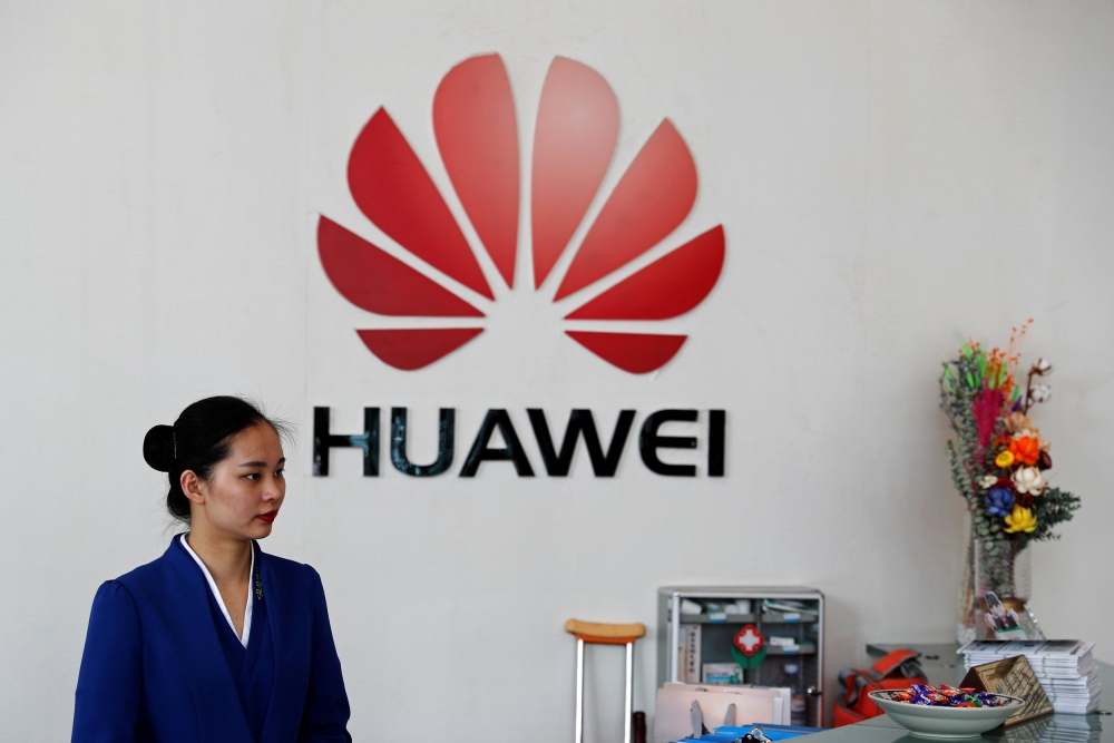 An employee stands next to the logo of Huawei in Shenzhen, Guangdong province, China, March 29, 2019. Reuters/Tyrone Siu