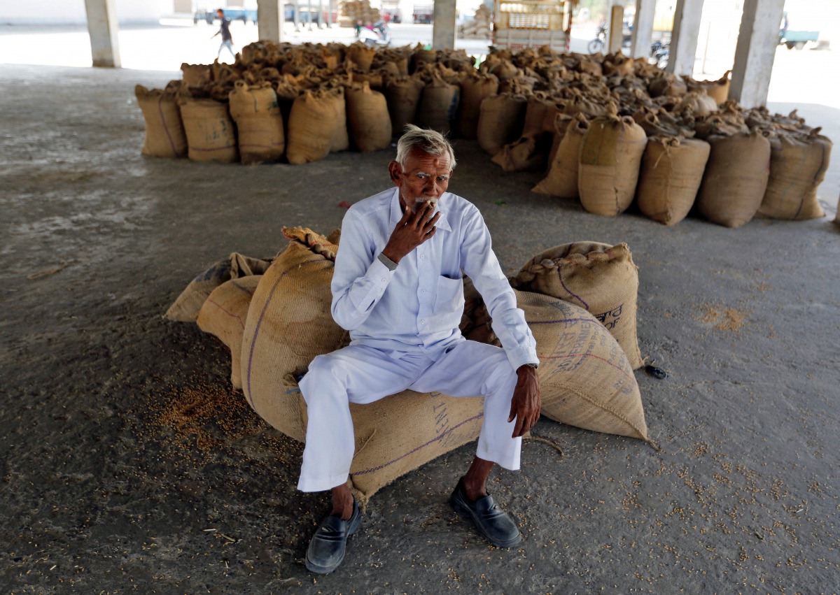 A farmer smokes while sitting on sacks of paddy crops as he waits for customers in Sanand village on the outskirts of Ahmedabad, November 15, 2016. Reuters