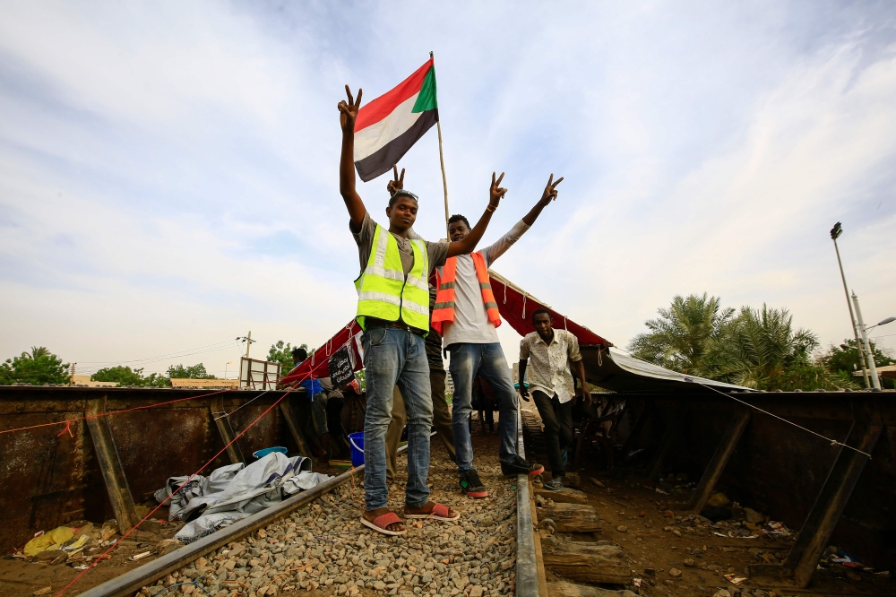 Sudanese protesters wearing yellow and orange gilets and waving a national flag stand on a closed railway track leading to the protest site in central Khartoum on May 12, 2019.   AFP / ASHRAF SHAZLY