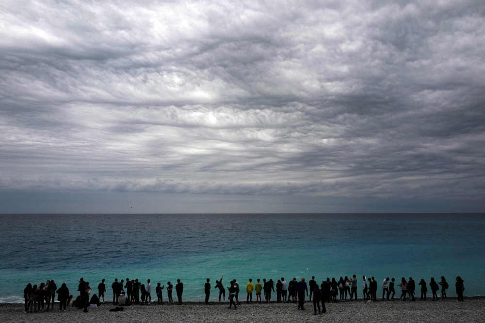 People stand on the beach in front of the Mediterranean Sea on the French Riviera city of Nice, on May 8, 2019. AFP / Valery Hache 