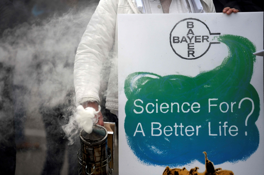 A protestor stands with a bee smoker and a placard reading 