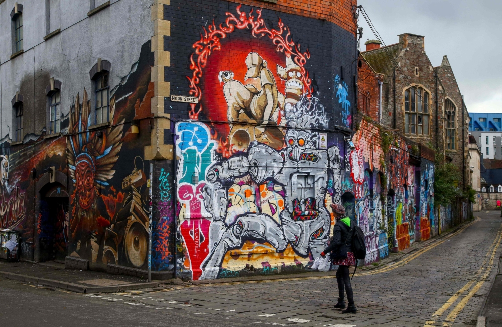 A pedestrian walks past graffiti street art on the side of a building in Bristol, south west England, on May 8, 2019.  AFP / Geoff Caddick 