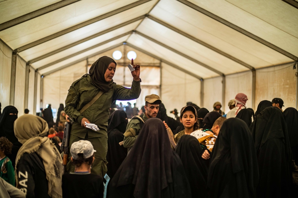 Fightres from the Syrian Democratic Forces (SDF) check the identities of displaced people before allowing them to board a bus waiting outside the Al-Hol camp in Al-Hasakeh governorate in northeastern Syria, on June 3, 2019, as Kurdish authorities started 