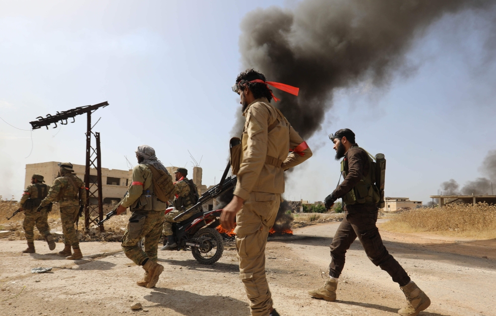 Fighters with the Turkish-backed National Liberation Front (NLF) hold a position near tyres set ablaze to create a smoke screen against air strikes by regime forces, in Syria's Hama province on June 6, 2019. / AFP / OMAR HAJ KADOUR